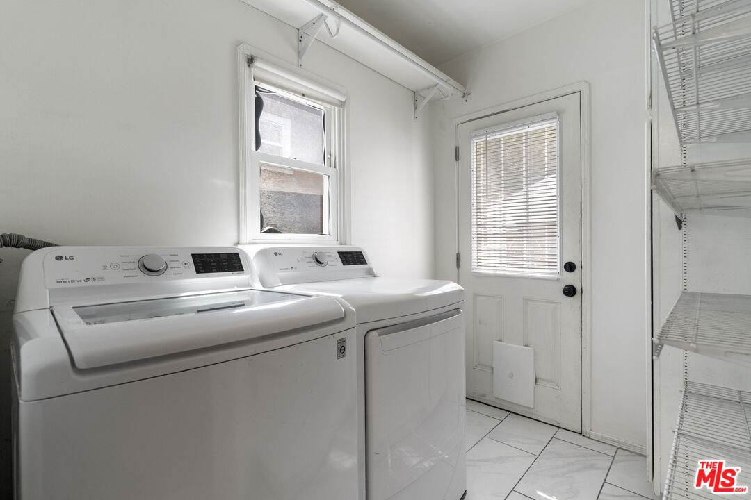 Laundry room with a white washer and dryer, window, and wire shelving.
