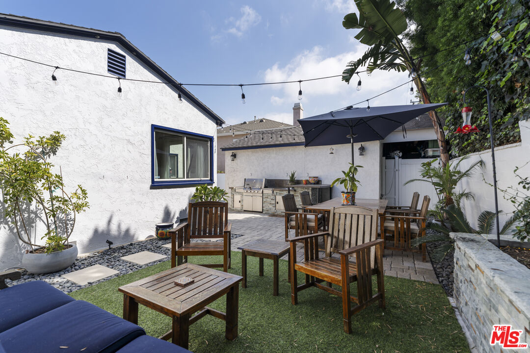 Backyard patio with wooden dining furniture, a large umbrella, and an outdoor grill.