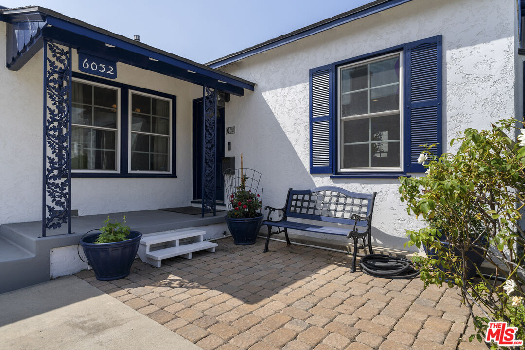 Home entrance with dark blue trim, a paved courtyard, potted plants, and a metal bench.