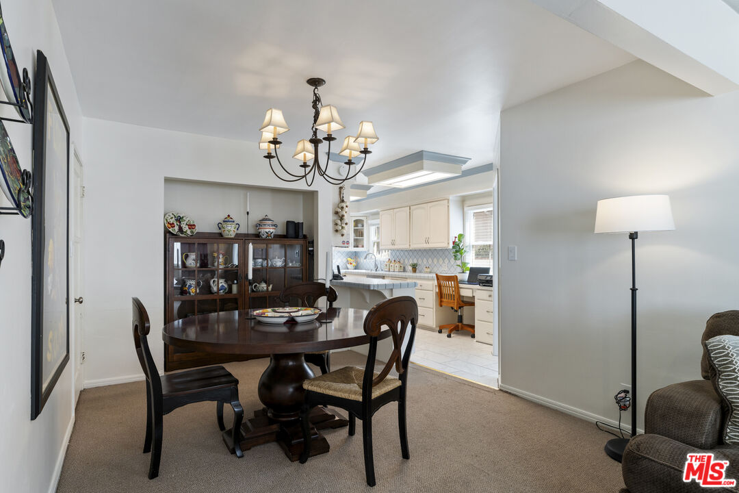 Dining room with a dark round table and china cabinet opening into a bright white kitchen.