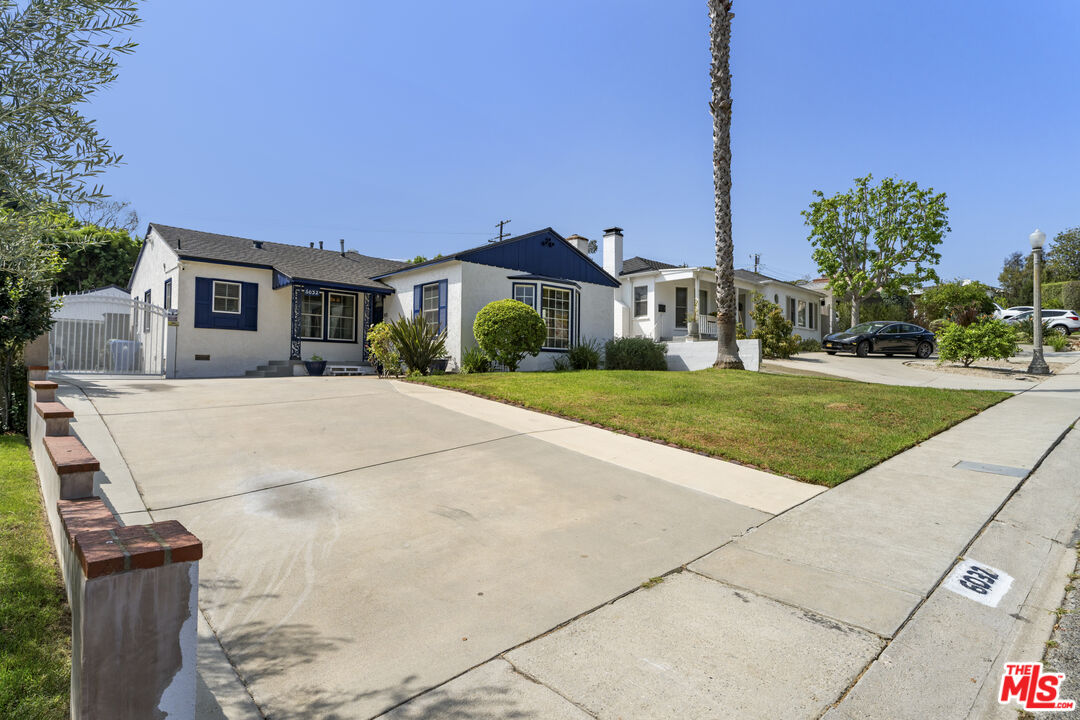 Single-story white stucco home with blue trim, a broad driveway, and a front lawn.