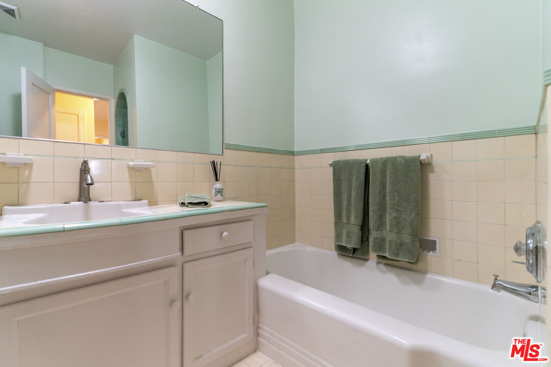 Bathroom with a white bathtub, cream tile, and pale green-trimmed vanity beneath a large mirror.