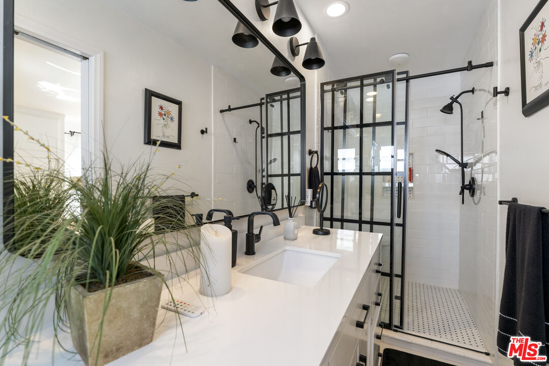 Bathroom with a black-framed glass shower, white tile, and a long vanity with black fixtures.