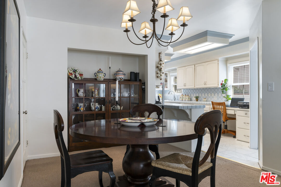 Dining room with a dark round table and chandelier, opening into a bright white kitchen.