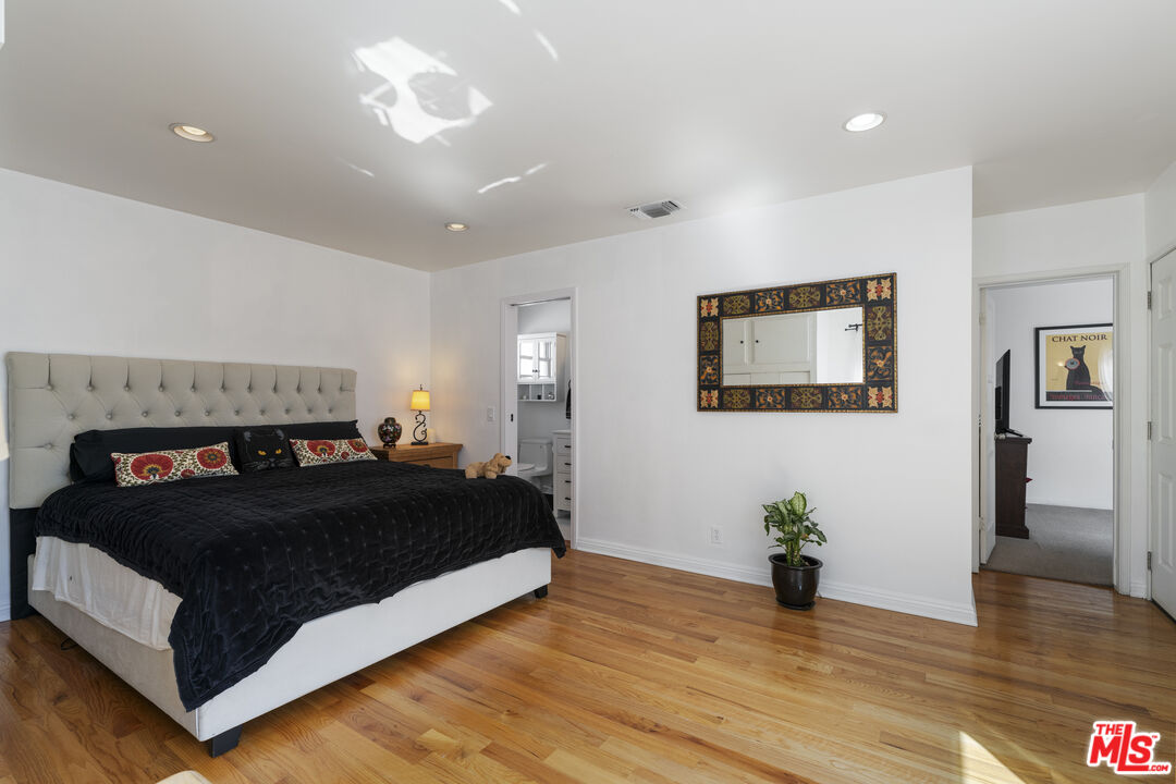 Bedroom with a tufted headboard, black bedding, hardwood floors, and a decorative mirror.