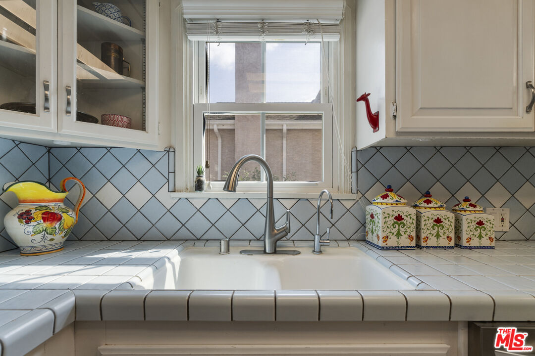 Kitchen sink beneath a window, framed by white tile and colorful ceramic containers.