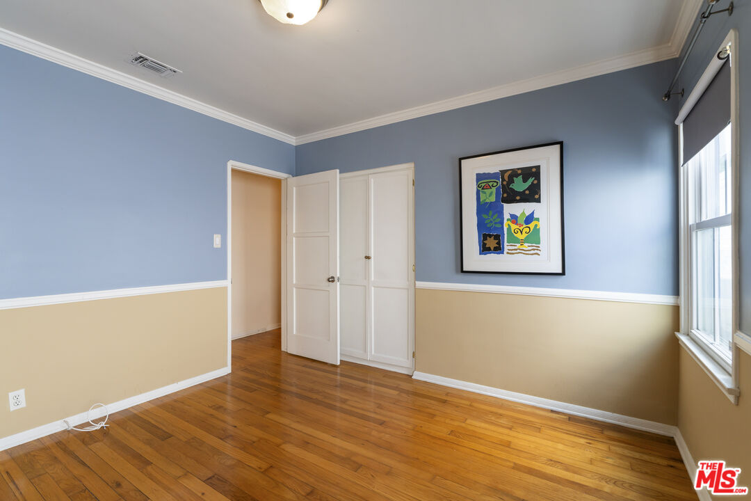 Empty bedroom with hardwood floors, blue and beige walls, an open closet door, and framed artwork.