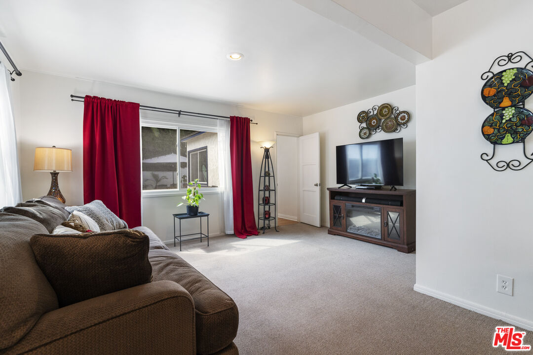 Living room with a brown sectional, red curtains, and a television on a wooden console.