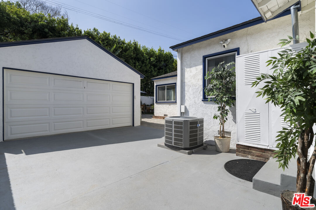 White stucco home and detached garage beside a broad concrete driveway and outdoor air-conditioning unit.