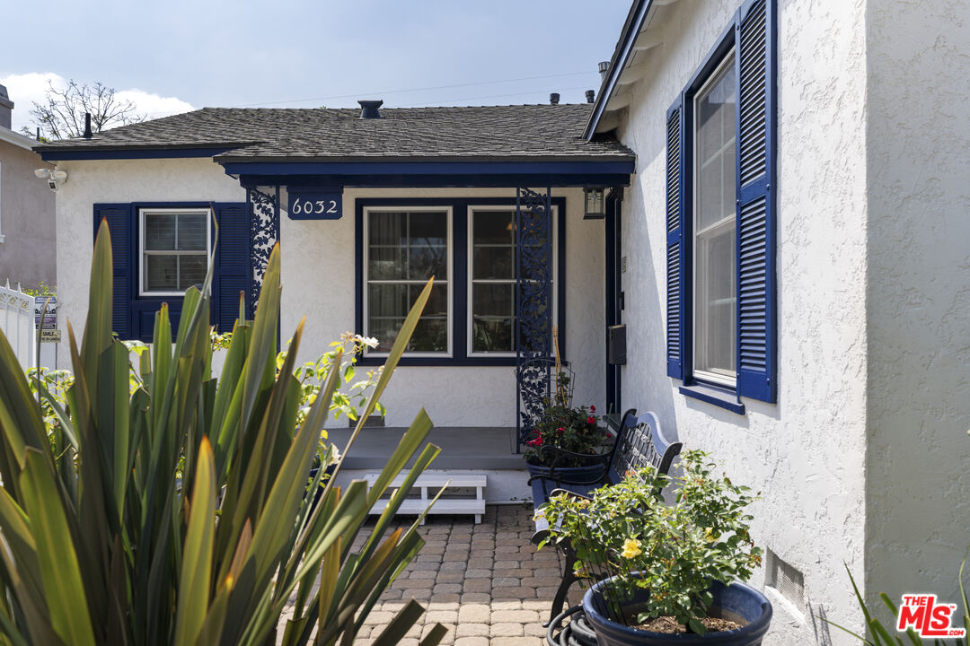 White stucco home with blue shutters, a covered entry, and a plant-filled paved courtyard.