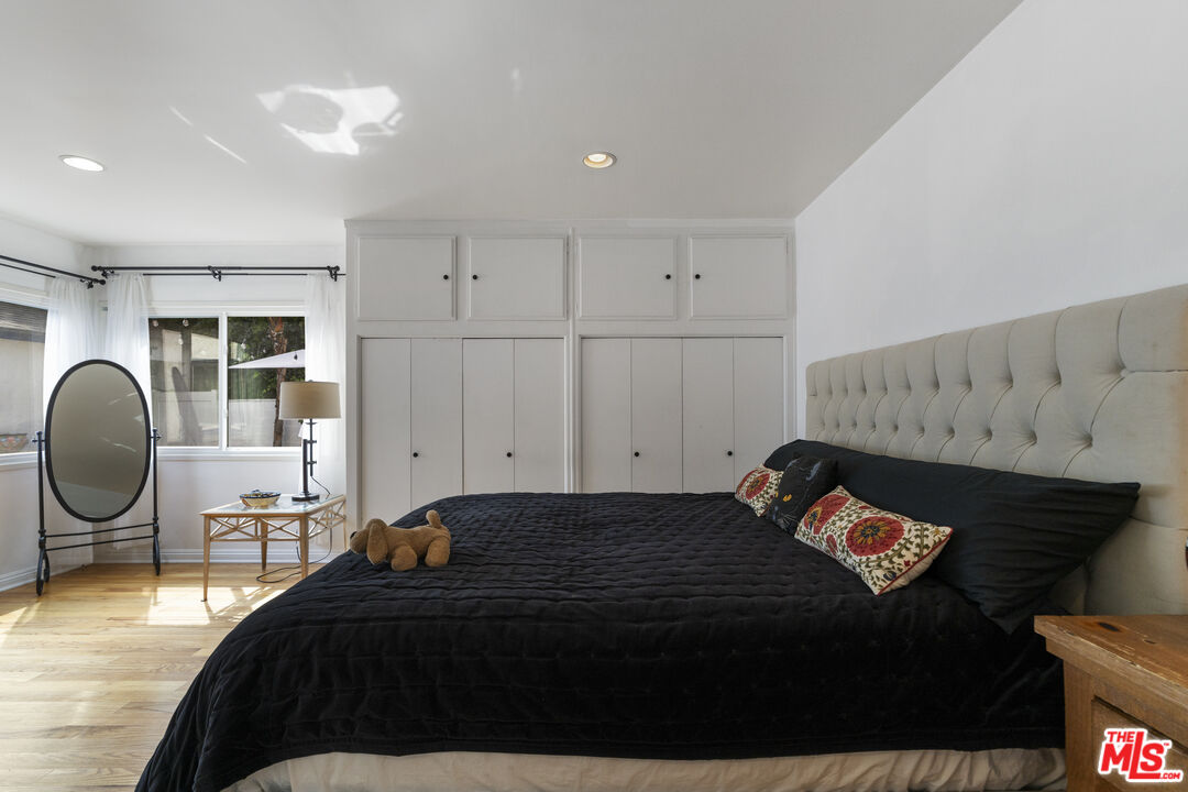 Bedroom with black bedding, a tall tufted headboard, built-in closets, and hardwood floors.