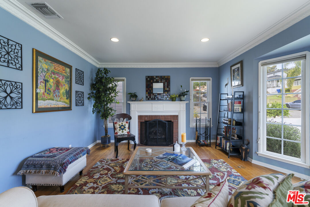 Living room with a white mantel and brick fireplace, blue walls, hardwood floors, and large windows.