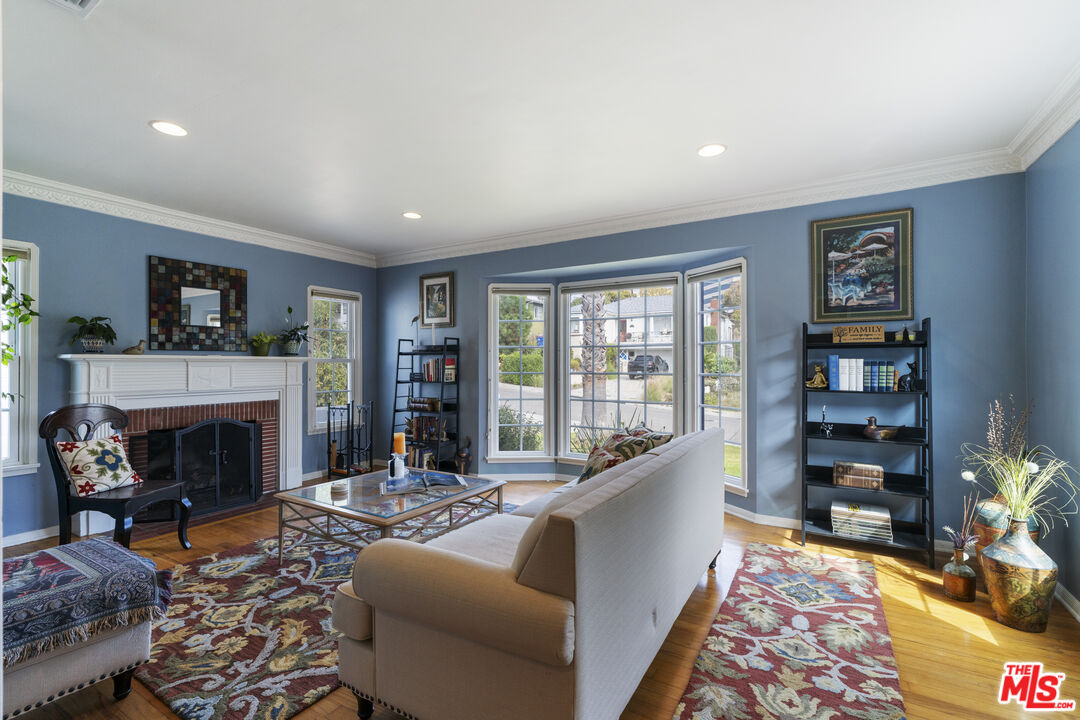 Furnished living room with a white fireplace, blue walls, large windows, and patterned rugs.