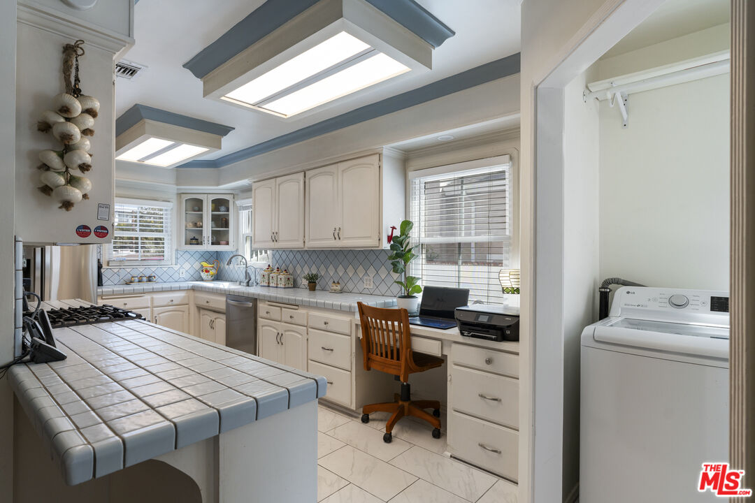 Kitchen with cream cabinets, tiled island, built-in desk, and adjoining laundry area.