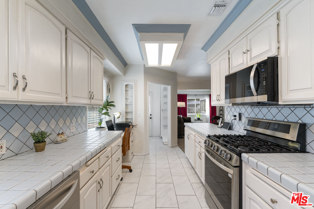 Galley kitchen with white tile counters, a diamond-pattern backsplash, and stainless steel appliances.