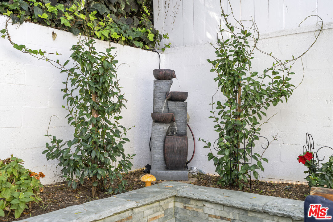 Tiered stone fountain surrounded by climbing vines and plants in a walled garden.