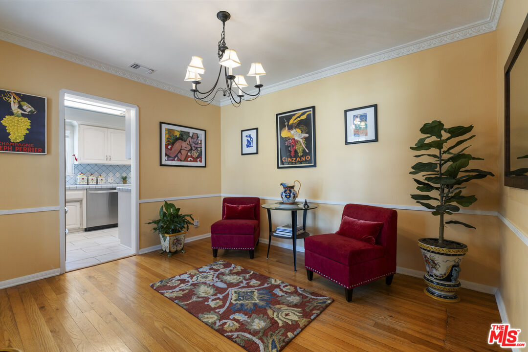 Sitting room with red chairs, a patterned rug, framed artwork, and a doorway to the kitchen.