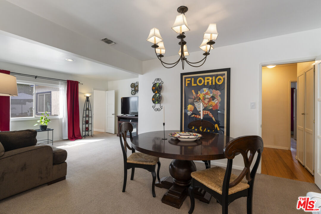 Dining and living area with a round wood table, chandelier, and large curtained window.