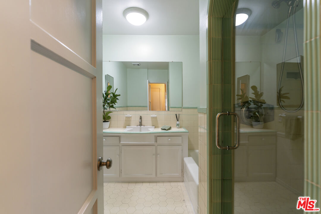 Bathroom with a white vanity, large mirror, hexagonal tile floor, and glass-enclosed shower.