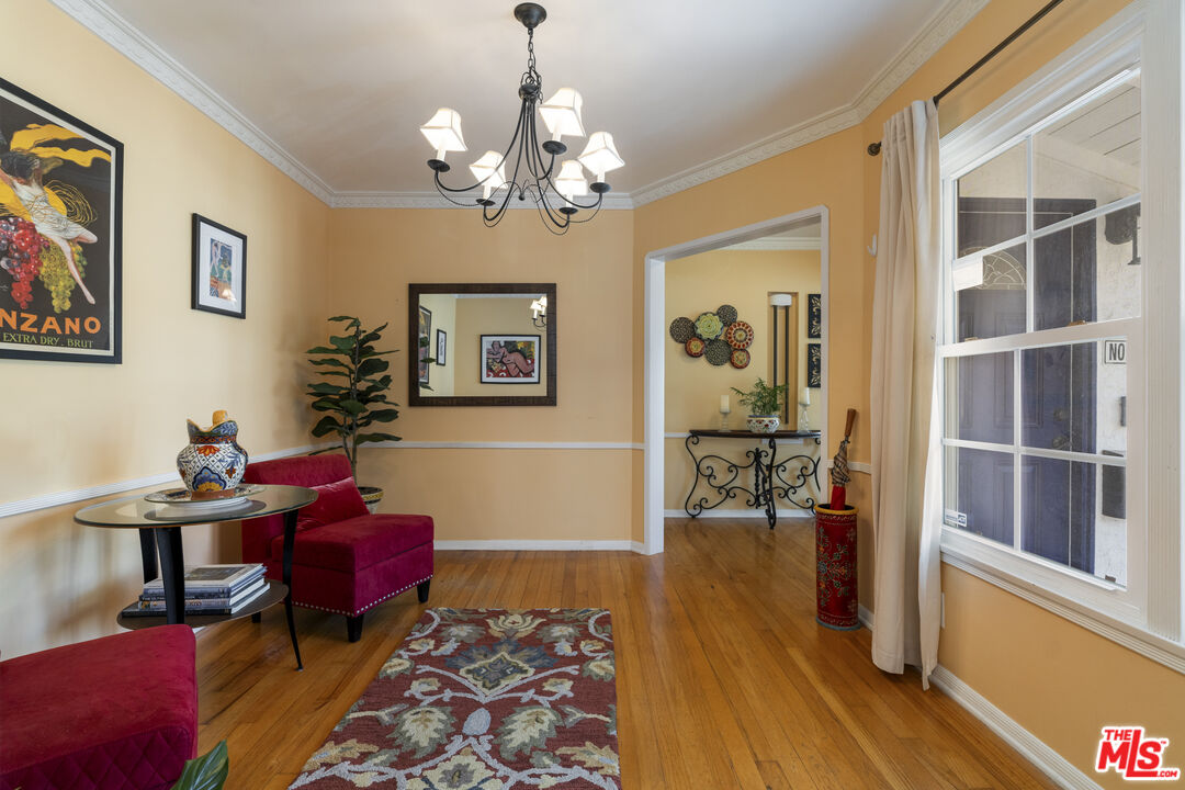 Sitting room with hardwood floors, red chairs, a chandelier, and a large window.