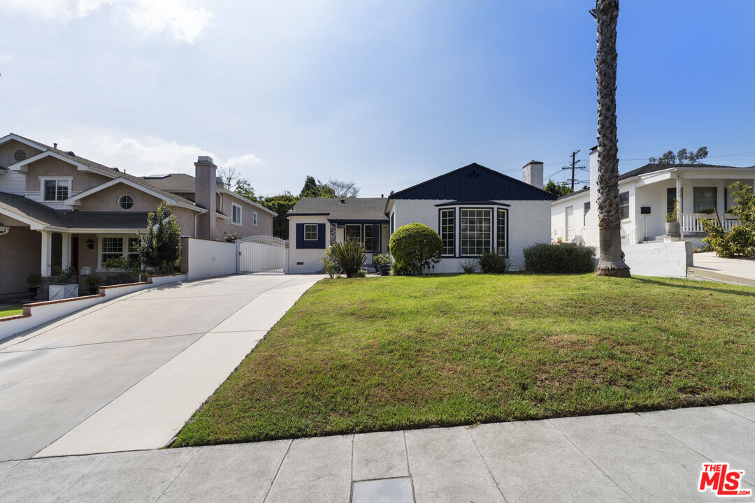 Single-story white house with a navy gabled roof, bay windows, lawn, and palm tree.