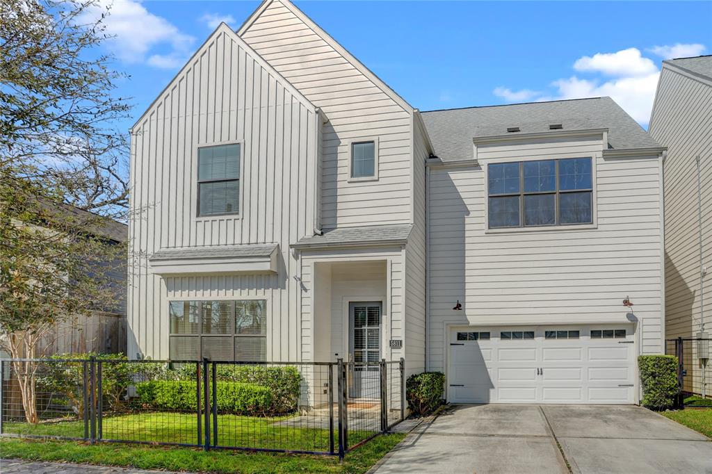 White two-story house with a steep gabled facade, attached garage, and fenced front yard.