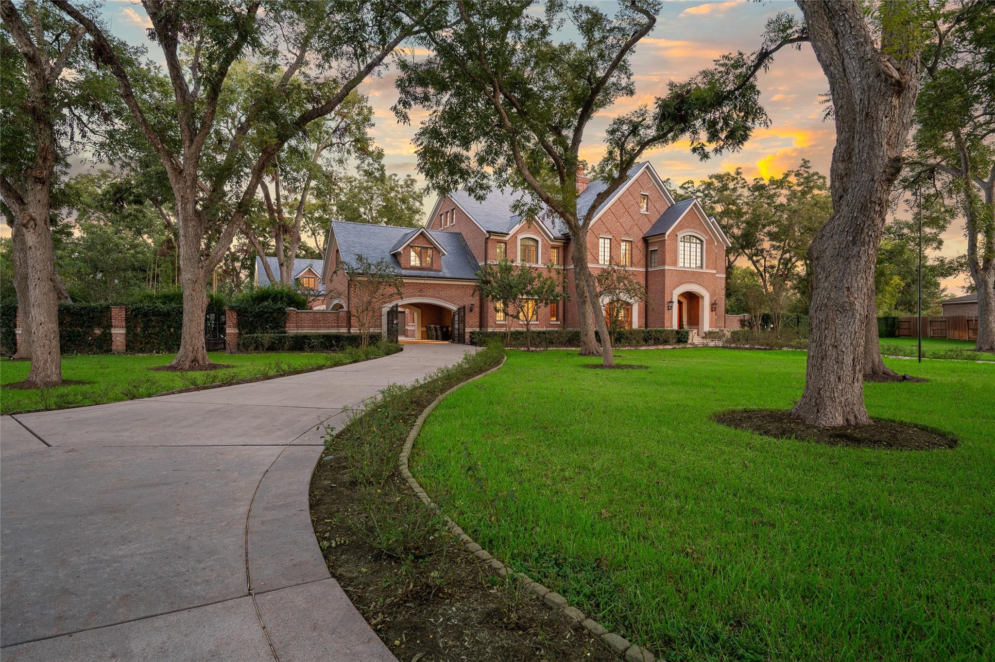 Two-story brick home framed by mature trees, with a curved driveway and expansive lawn.