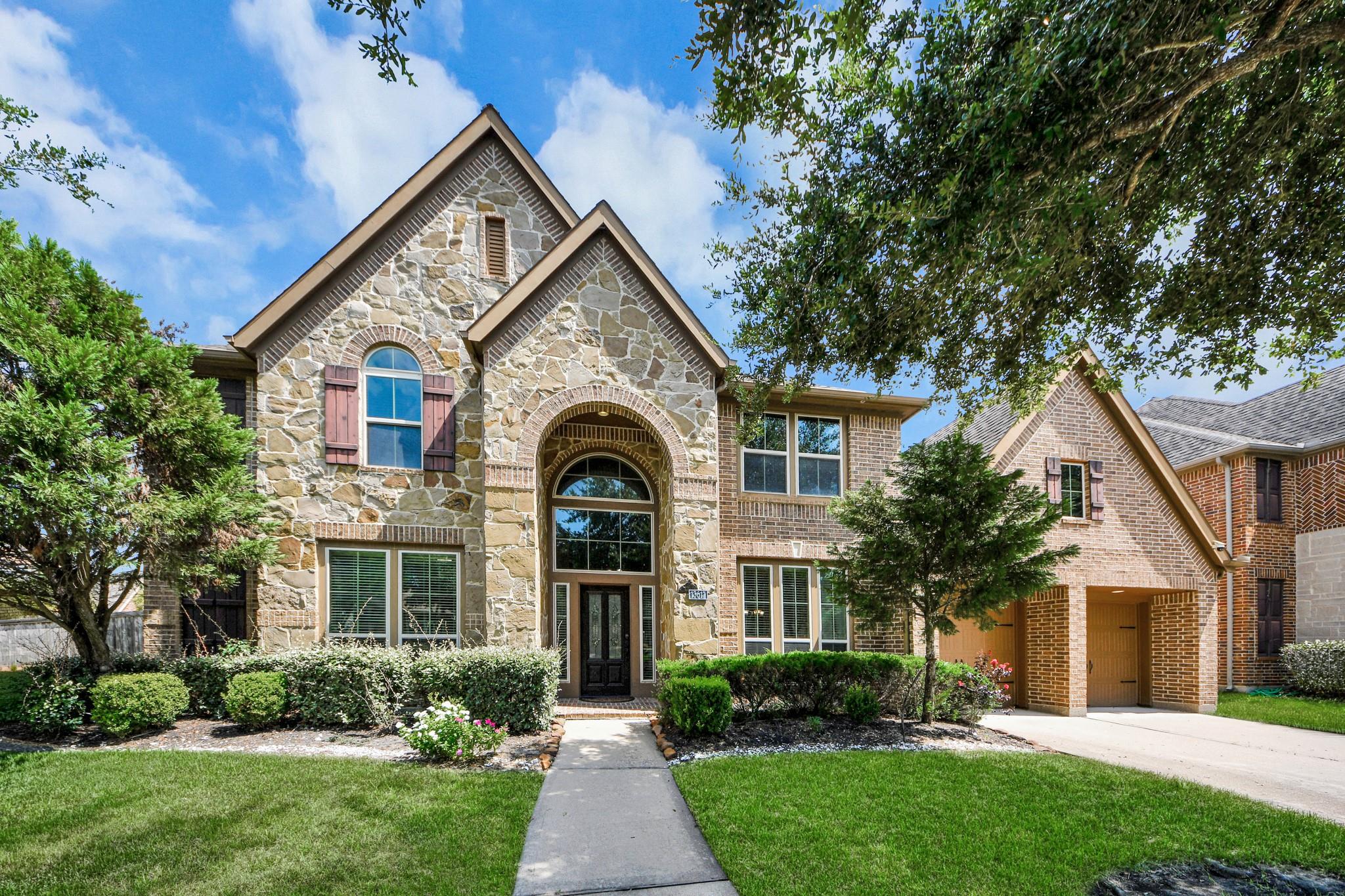 Two-story stone-and-brick home with an arched entry and landscaped front yard.