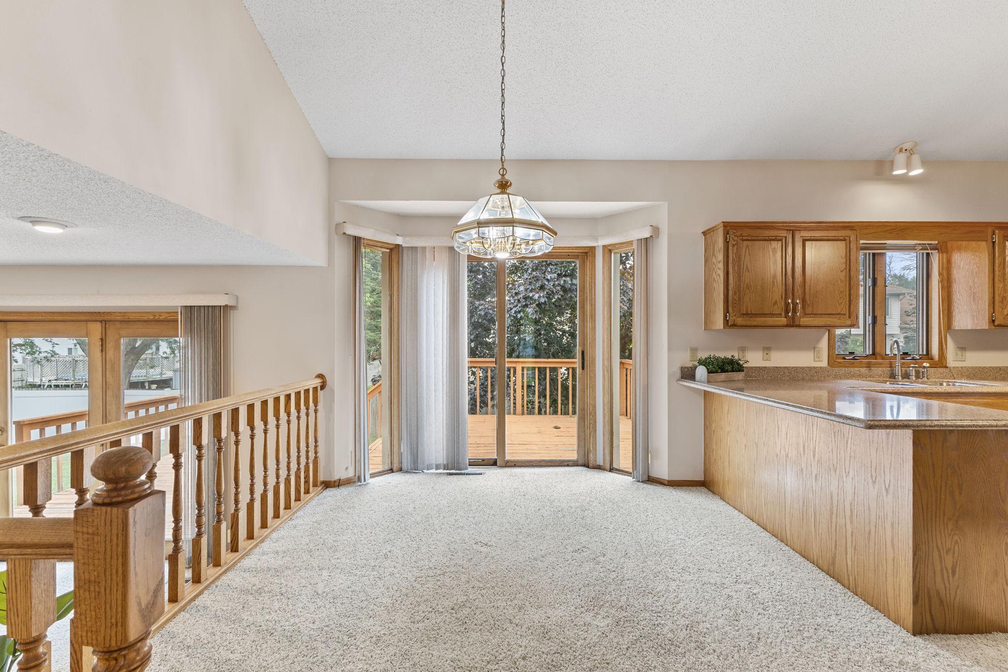 Empty dining area with a chandelier, wood-cabinet kitchen, and sliding doors to a deck.