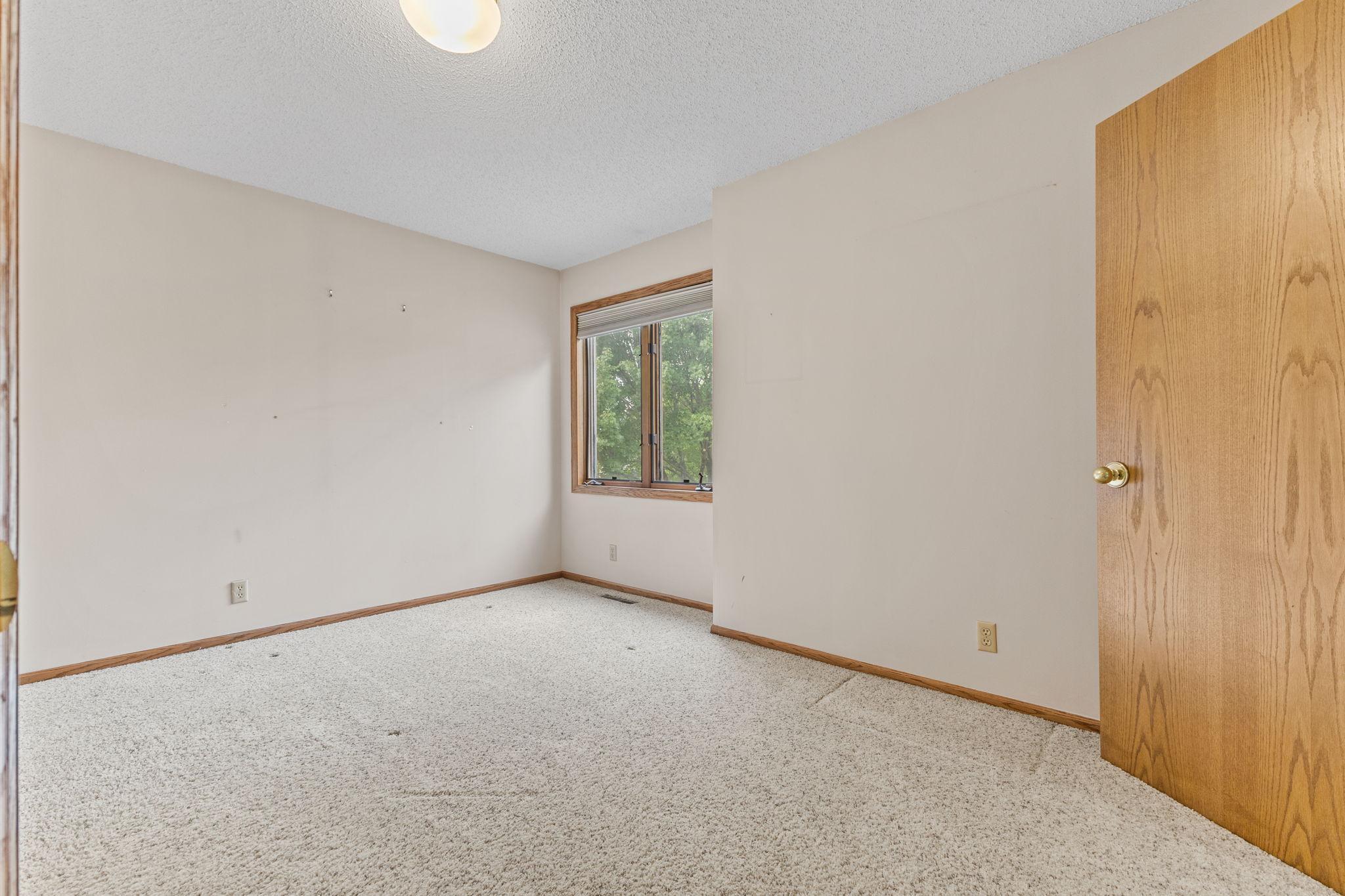 Empty carpeted room with wood trim, a window overlooking trees, and an open wooden door.