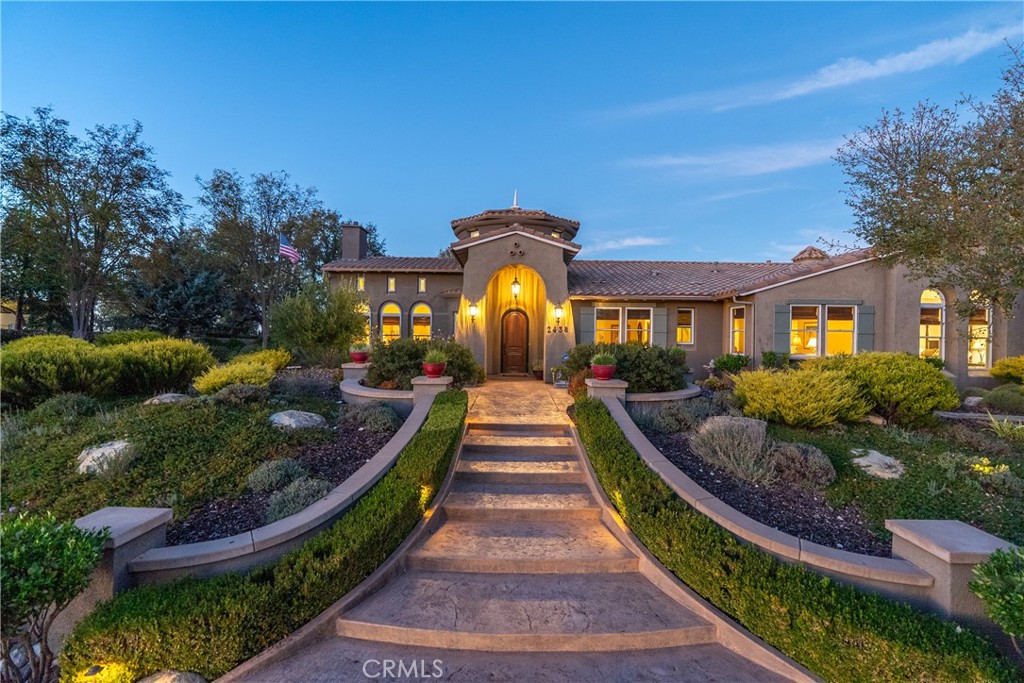 Stucco home at dusk with a warmly lit arched entrance and landscaped stone walkway.