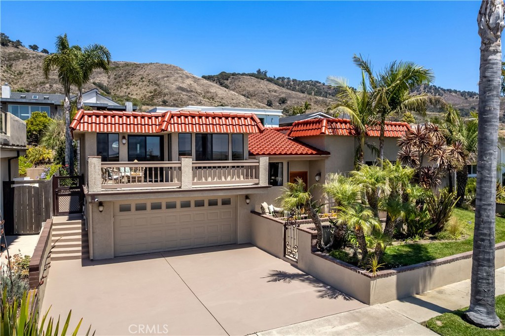 Two-story beige house with red tile roofs, a balcony, attached garage, and palm landscaping.