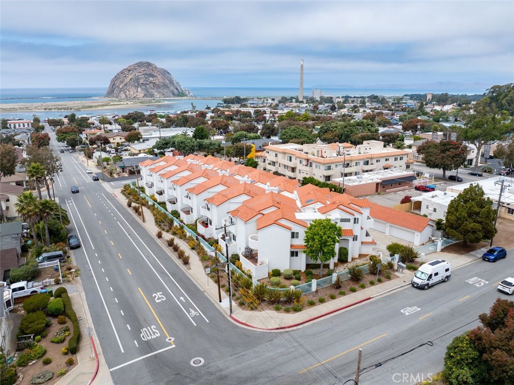 Aerial view of white terracotta-roof townhomes beside the coast, with Morro Rock across the bay.