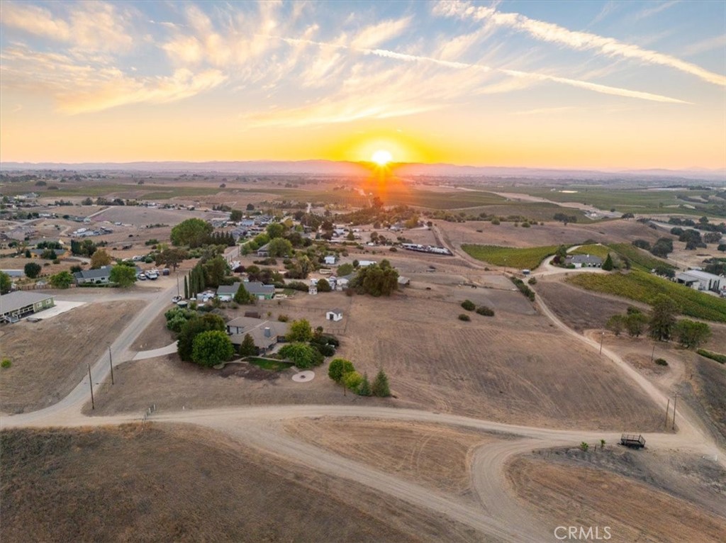 Aerial view of a rural home and surrounding fields at sunset, with outbuildings and a dirt road.