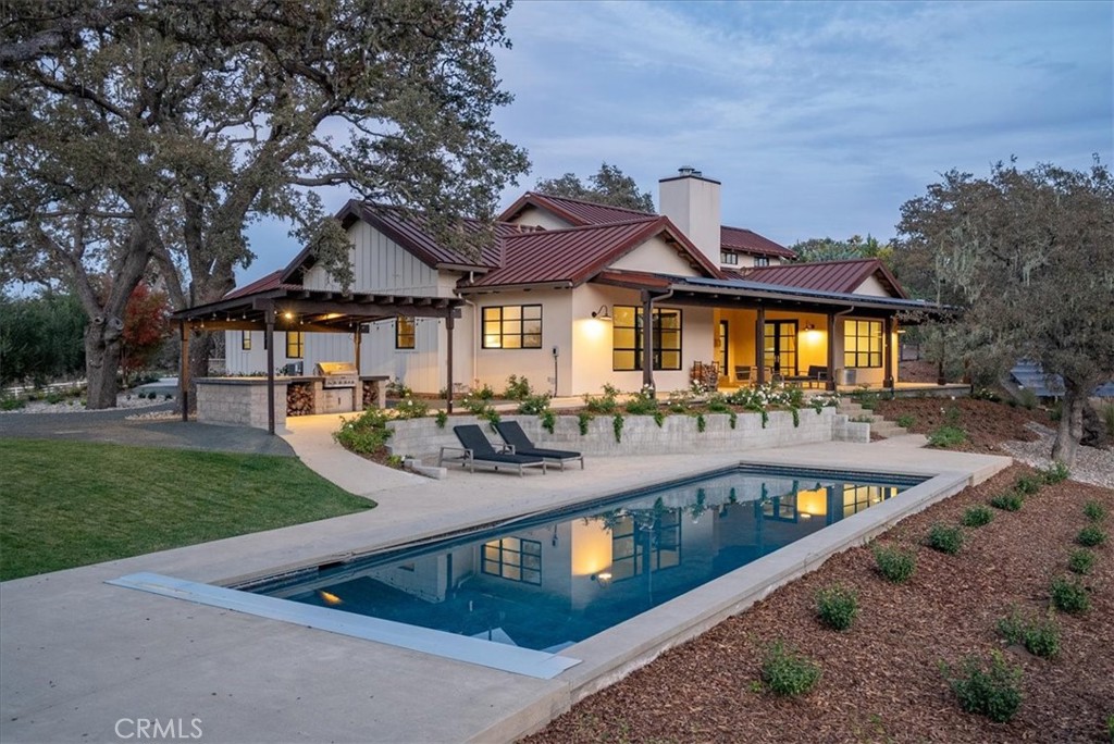 Home with a red metal roof and covered patio beside a swimming pool at dusk.