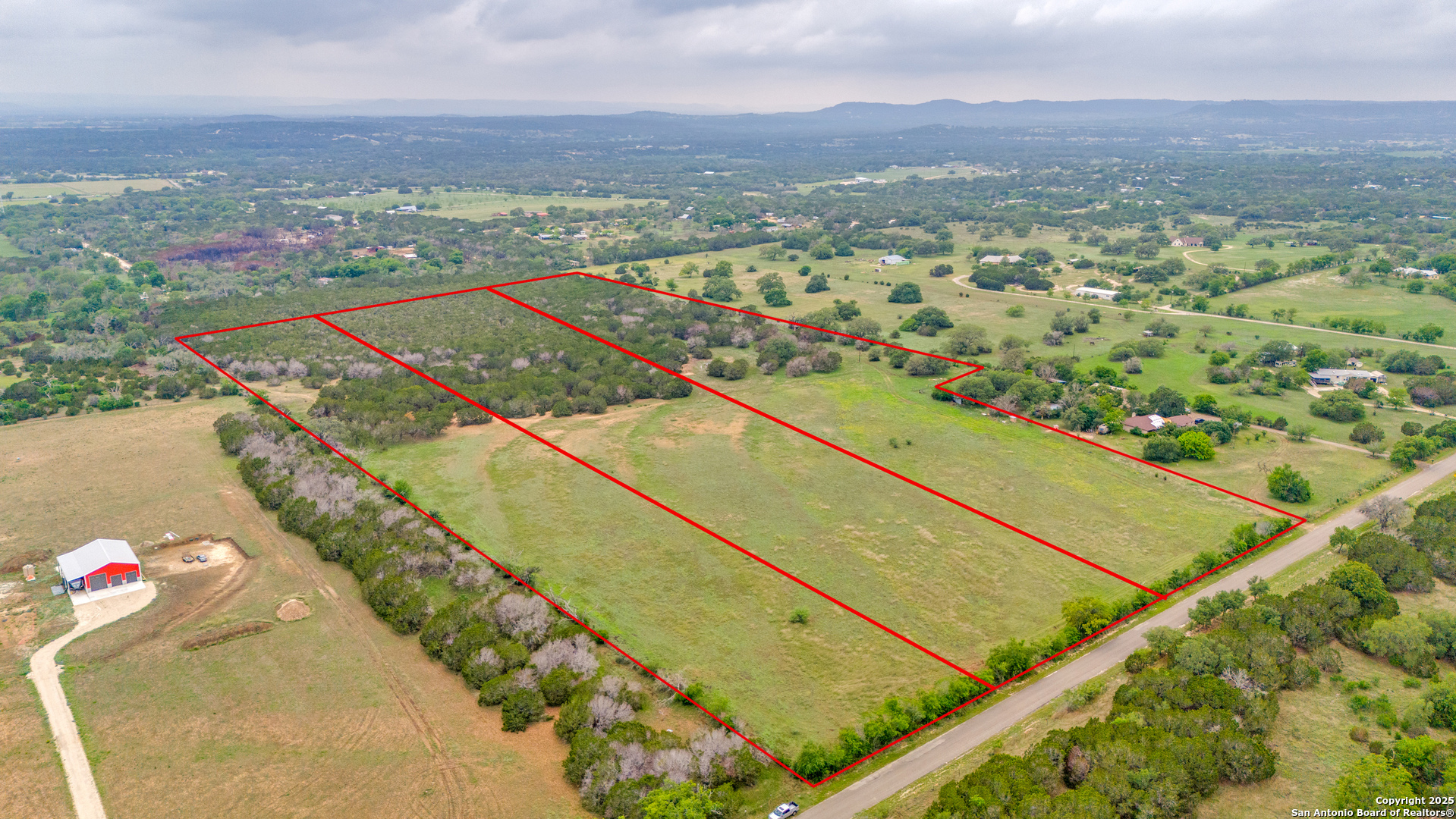 Aerial view of grassy rural parcels outlined in red, with wooded areas and paved road frontage.