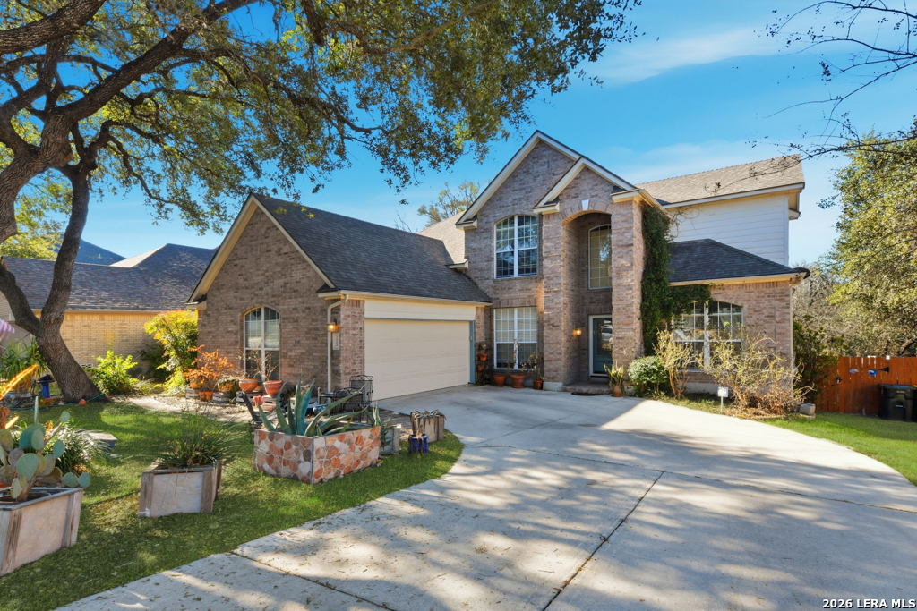 Two-story brick house with an attached garage, broad driveway, and mature oak tree.