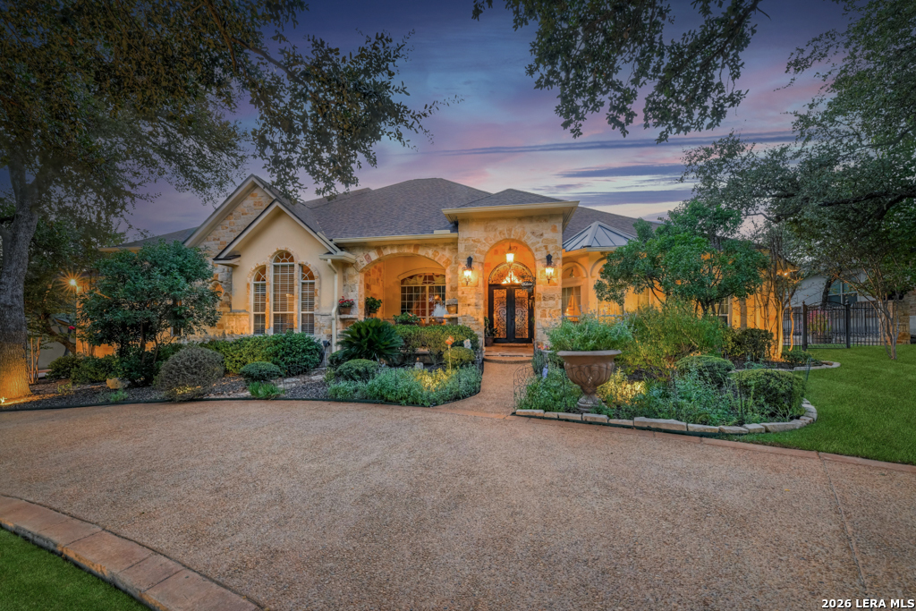 Stone-and-stucco home with a landscaped garden and curved driveway at dusk.