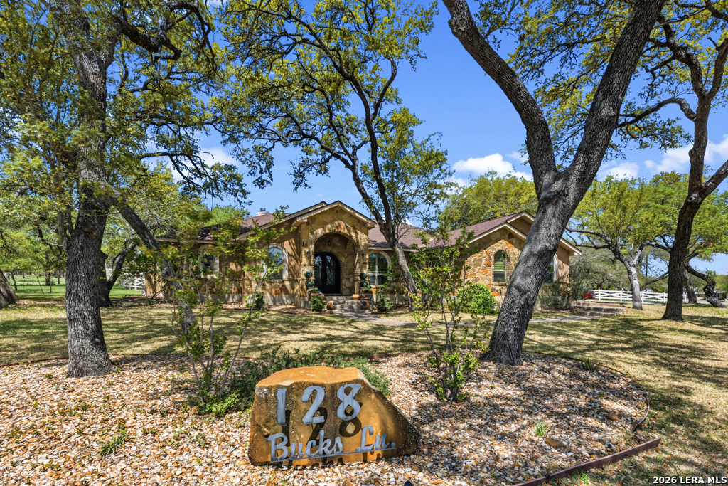 Stone-front home framed by mature trees, with a rock address marker reading 128 Bucks Ln.
