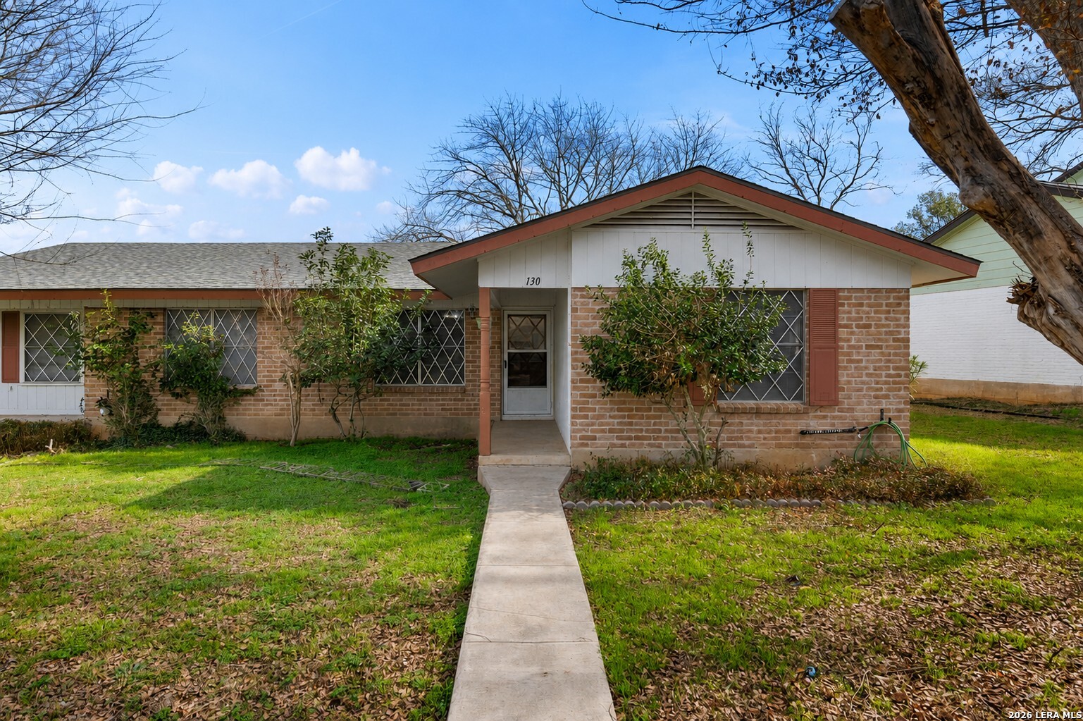 Single-story brick house with a white entry porch and a straight concrete walkway through the lawn.