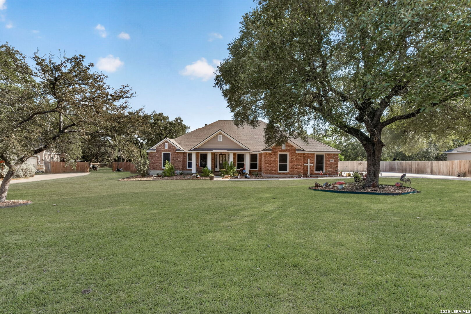 Red brick single-story house with a covered porch, broad lawn, and mature shade trees.