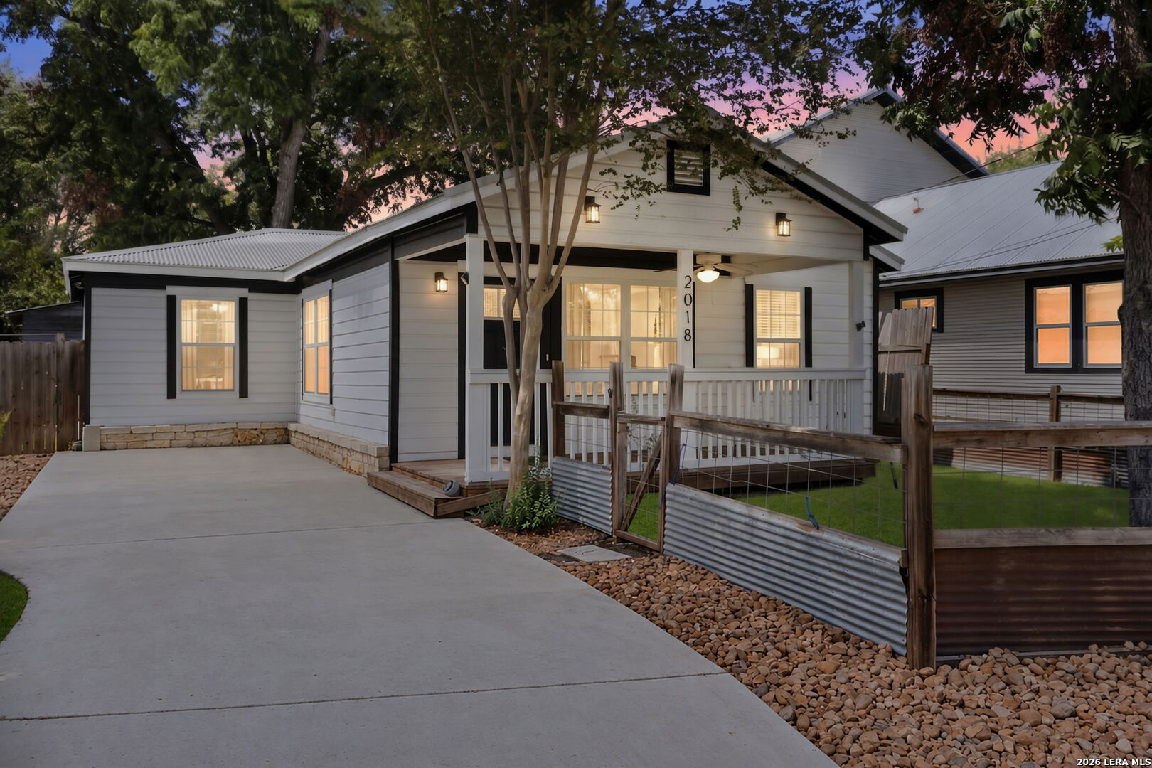 White single-story home with dark trim, a covered porch, and a broad concrete driveway at dusk.