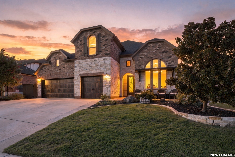 Two-story brick and stone house at dusk with a double garage and arched window.
