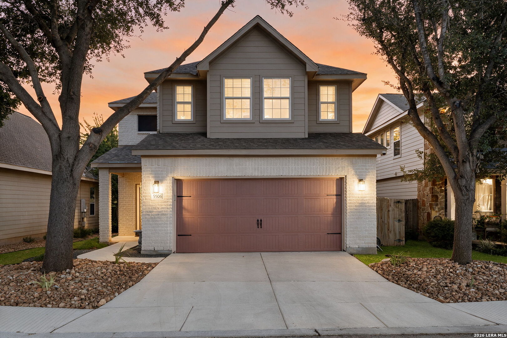 Two-story gray house with a wide garage, framed by mature trees at dusk.