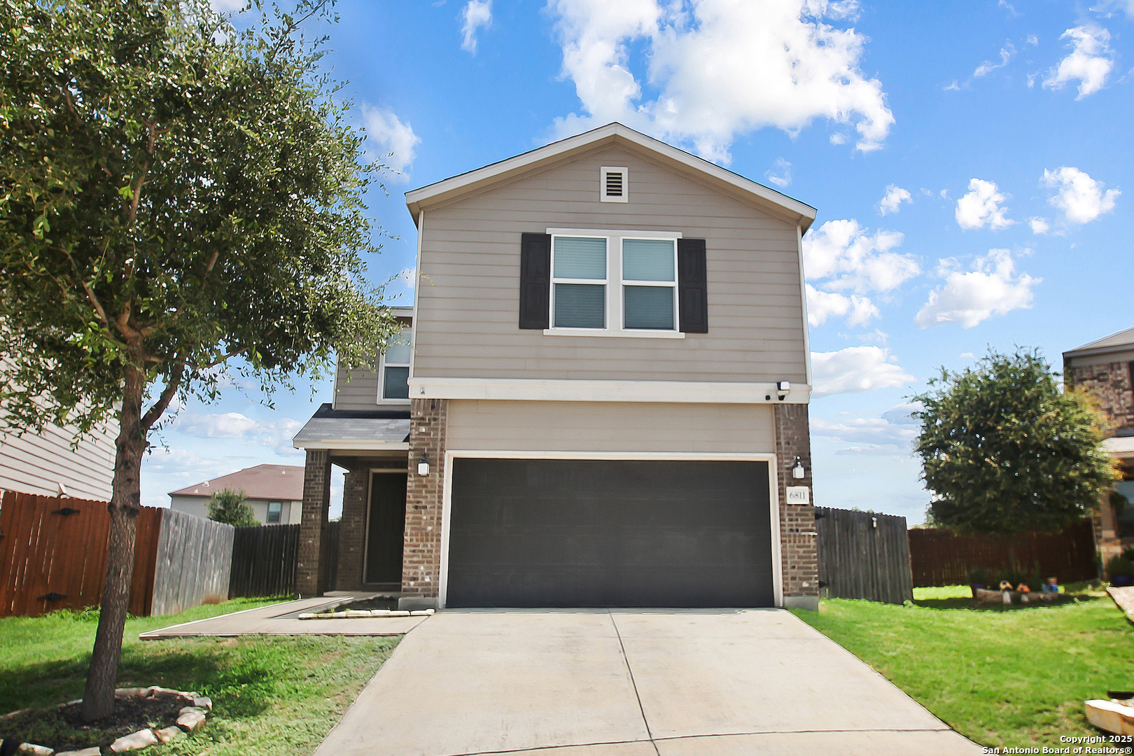 Two-story beige house with brick accents, a wide garage, and a concrete driveway.
