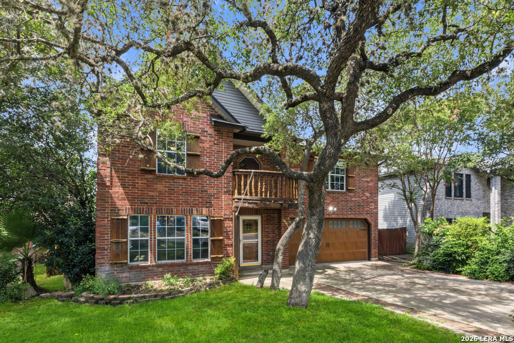 Two-story red brick house with a wooden balcony, attached garage, and mature trees in front.
