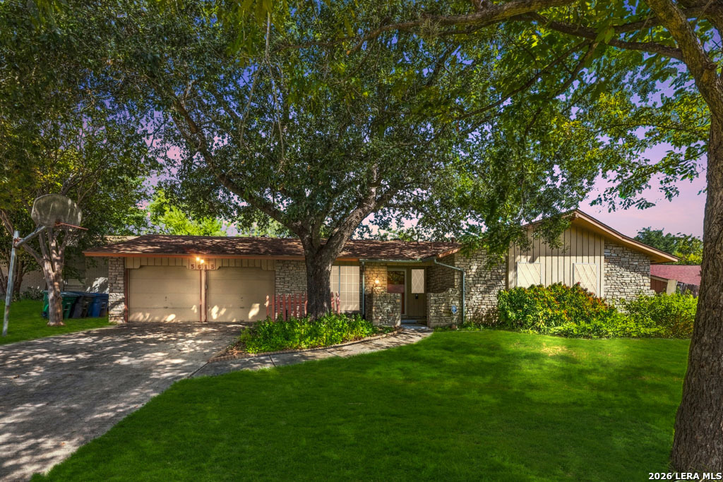 Single-story stone house with a two-car garage beneath a large shade tree.