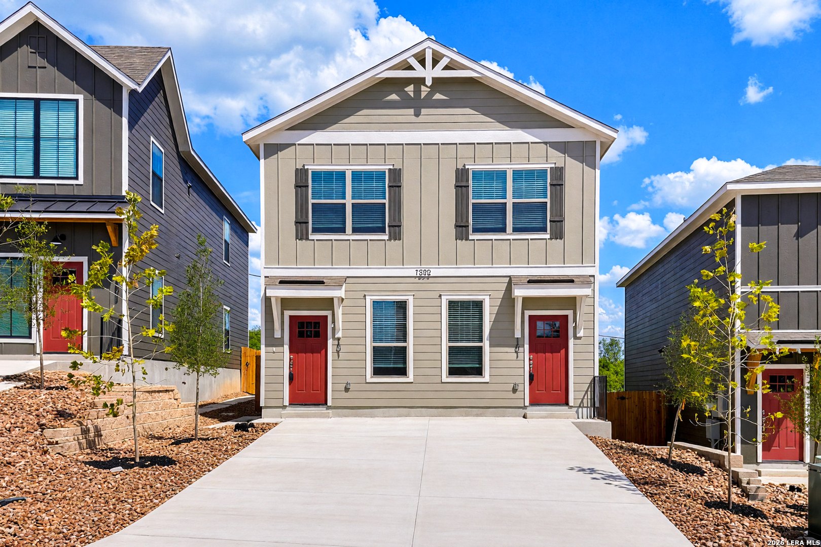 Two-story gray home with twin red entry doors and a broad concrete driveway.