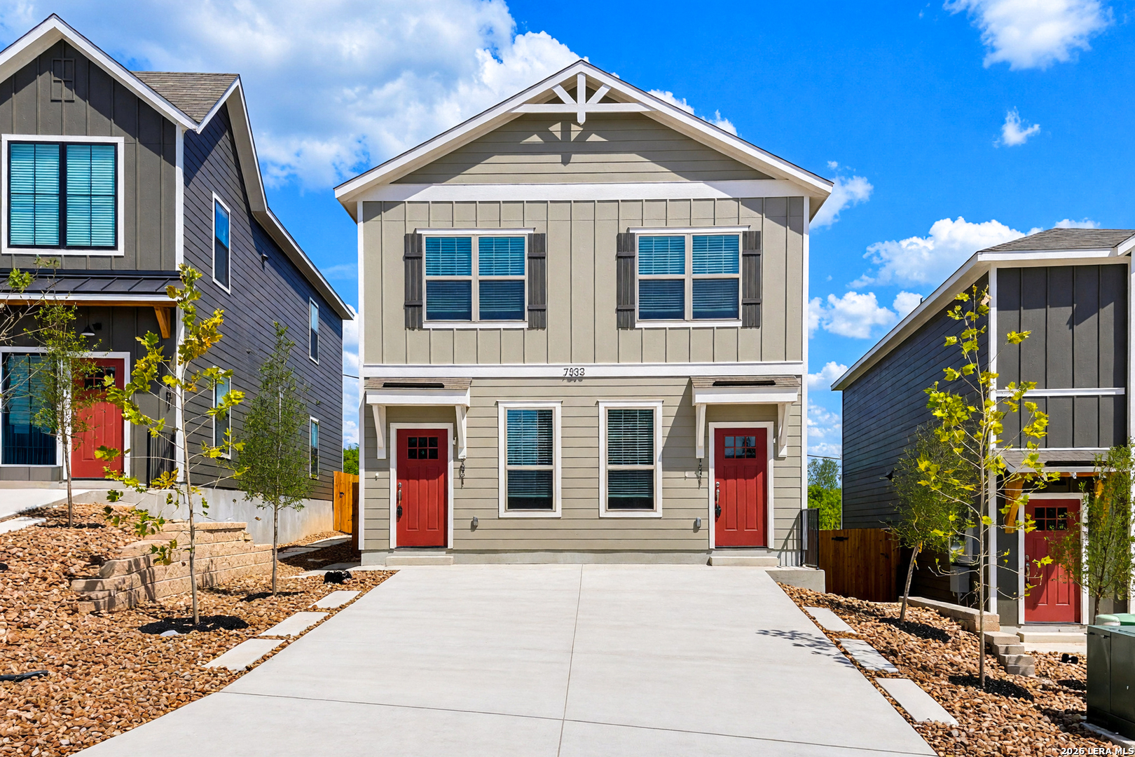 Two-story gray duplex with red front doors, white trim, and a wide concrete driveway.