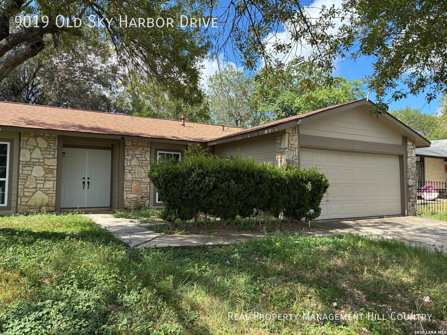 Single-story home with stone accents, an attached garage, and mature trees shading the front yard.